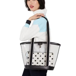 A woman is carrying a transparent tote bag with black accents and a polka dot pouch inside. She is wearing a white and light blue top.