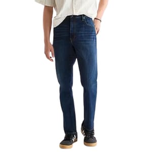 A person is wearing dark blue jeans, a light-colored shirt, and black sneakers with gum soles.