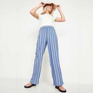 A person wearing a white sleeveless top and blue striped wide-leg trousers with black open-toe slides.