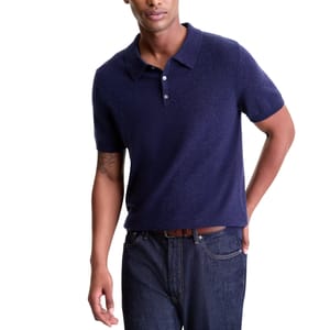 A man is wearing a navy blue short-sleeve polo shirt paired with dark jeans and a brown belt.