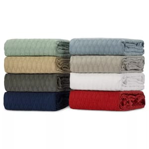 A stack of folded quilts in various colors including green, blue, beige, gray, white, and red.