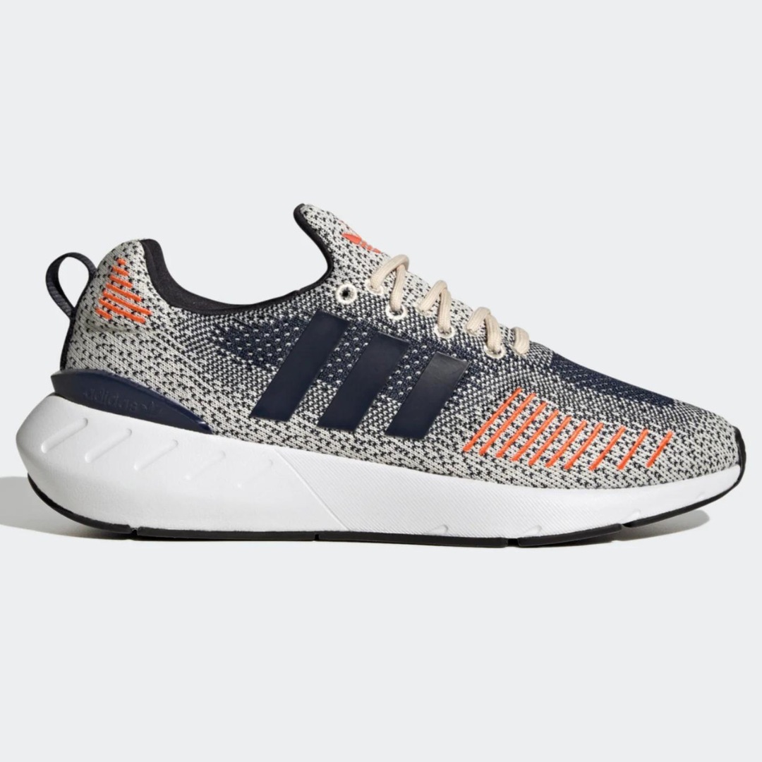 A single gray and white sneaker with orange accents and black stripes.
