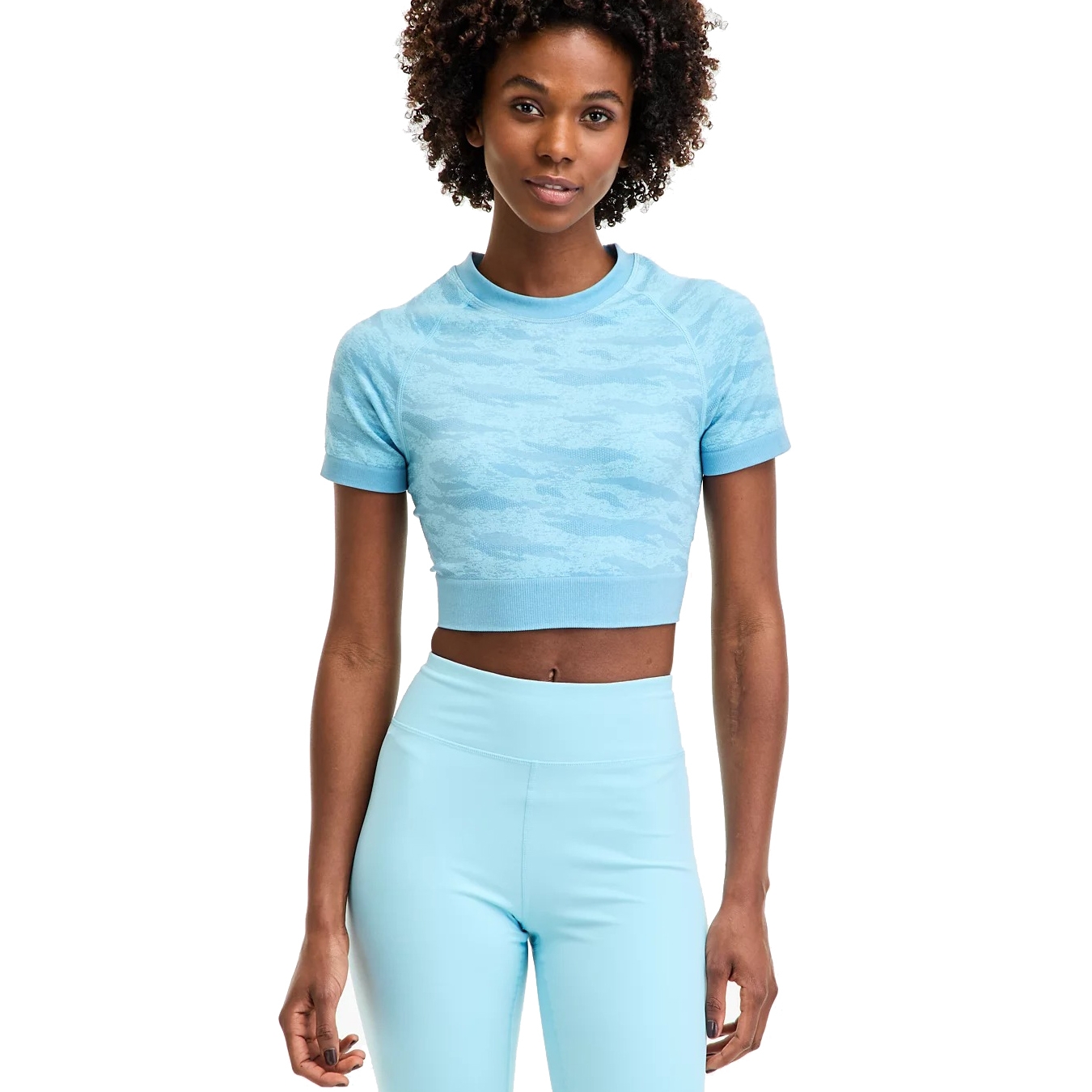 A person wearing a light blue, short-sleeve, cropped athletic top with a subtle camouflage pattern and matching high-waisted leggings.