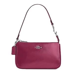 The Coach Nolita 19 is a compact burgundy leather bag with a short strap and a secure zip closure. It features the Coach logo in metallic lettering on the front and includes a small hanging tag.