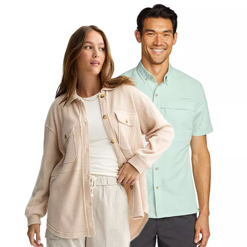 A woman in a beige, button-up, textured overshirt paired with light pants stands next to a man wearing a light green short-sleeve shirt and dark pants.