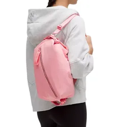 A person wearing a gray hoodie and black leggings carries a pink Lululemon backpack-style bag over their shoulder.