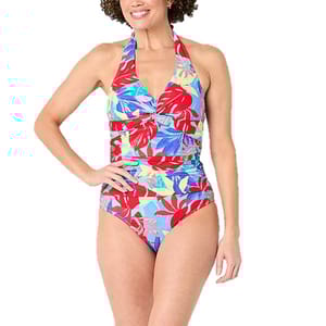 A woman is wearing a vibrant one-piece swimsuit with a halter neck and a colorful tropical leaf pattern in red, blue, and green tones.