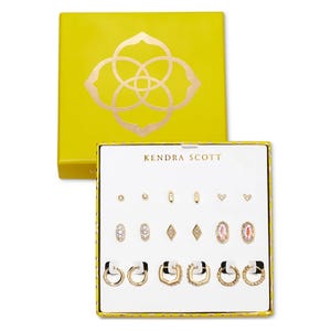 Kendra Scott jewelry set in a yellow box featuring various gold earrings, including studs, hoops, and decorative designs.