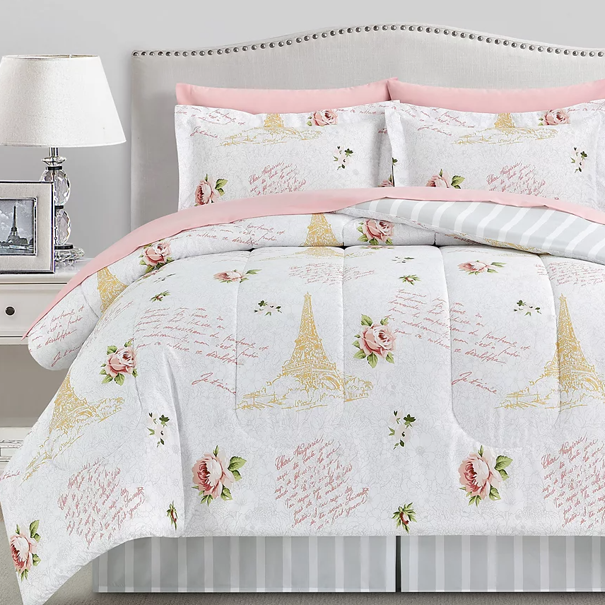 8-piece Paris & Floral Comforter Set features a design with Eiffel Tower motifs, pink roses, and cursive script on a white background. Includes a comforter, shams, sheets, and a bed skirt, accented with pink edges and stripes for a chic look.