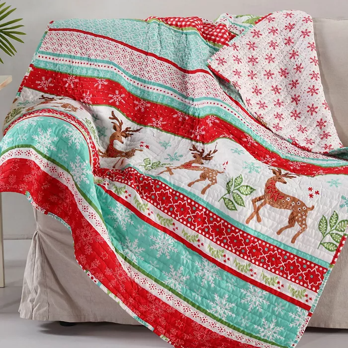 A colorful Christmas-themed quilt draped over a chair, featuring red, green, and white stripes, reindeer, snowflakes, and leaf patterns.