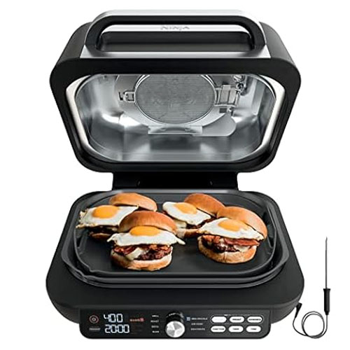 An open Ninja Grill & Griddle with eggs and sandwiches cooking on the griddle, accompanied by a temperature probe on the side.