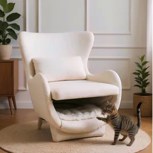A cozy cream-colored chair with a built-in pet bed at its base sits on a circular rug, while a tabby cat plays nearby. The setting is accented with green plants and a wooden cabinet.