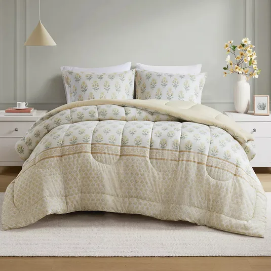 A bed is dressed with a floral-patterned comforter and matching pillowcases. The set is complemented by a simple white nightstand, a neutral pendant light, and a vase with yellow flowers.