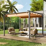 A 12' x 10' pergola with a retractable canopy provides shade over an outdoor seating area with woven chairs and a sofa around a coffee table. The setup is on a patio beside a modern house, featuring lush greenery and palm trees in the background.