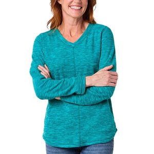 A woman is wearing a teal long-sleeve shirt with a V-neck design, paired with blue jeans. Her arms are crossed in front of her.