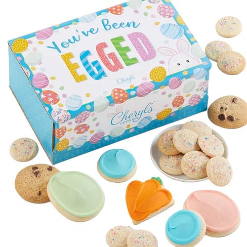Colorful box of Cheryl’s cookies with designs and text \“You've Been Egged,\“ including chocolate chip, sugar cookies with frosting, and an orange carrot-shaped cookie.