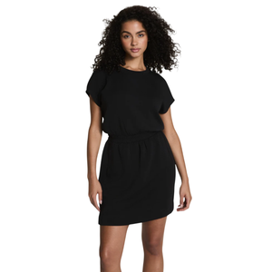 A woman with curly hair wears a short-sleeved black dress with a cinched waist and short hem, standing against a plain background.