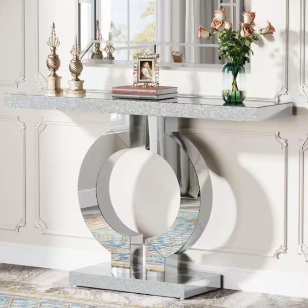 A sleek console table with a shimmering top and distinctive circular metallic base, adorned with decorative items including books, a framed photo, and a vase with roses against a paneled wall.