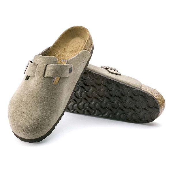 A pair of taupe suede clogs with a slip-on design, featuring a buckle and textured black rubber soles.