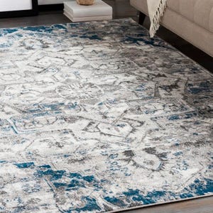 A 5' square area rug features a distressed design with intricate patterns in gray, white, and blue hues, adding a modern and stylish touch to the room's decor.