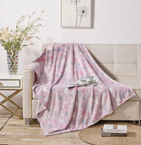 A pink throw blanket with heart and star patterns draped over a couch, with a cup and saucer on top.