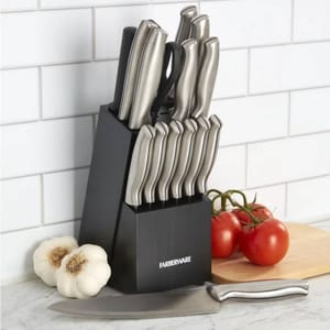 Farberware 15-piece knife set with a black block, featuring stainless steel handles. Includes various knives for different purposes, such as a chef's knife, bread knife, and paring knives. Garlic and tomatoes are set nearby for context.