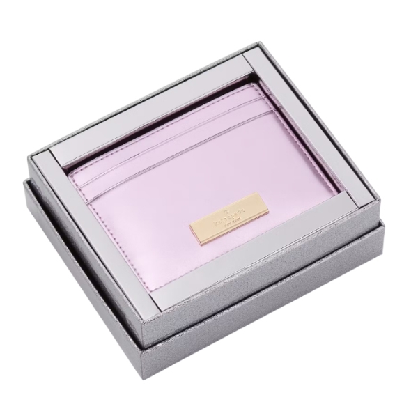 A lavender-colored Kate Spade card holder packaged in a silver gift box, featuring multiple slots and accented with a gold-toned nameplate.