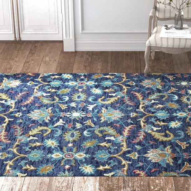 A blue floral-patterned area rug on a wooden floor, with a decorative chair and vase in the background.