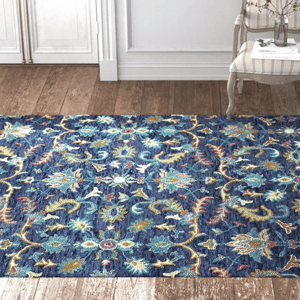 A blue floral-patterned area rug on a wooden floor, with a decorative chair and vase in the background.