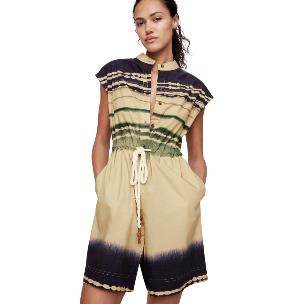 A woman is wearing a short-sleeved romper with a button-up front and a drawstring waist, featuring a tie-dye pattern in shades of beige, green, and dark blue.