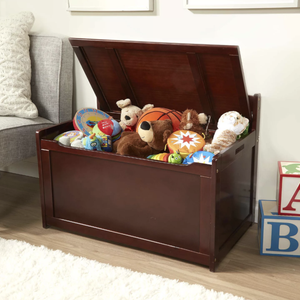 A wooden toy chest filled with various toys, including plush animals, a basketball, and colorful stuffed items. The chest is placed next to a sofa, with alphabet blocks on the floor nearby.