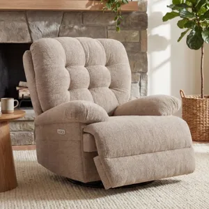 A beige, tufted, upholstered recliner sits on a cream rug next to a wooden side table with a mug and books. A stone fireplace with a wooden mantel adorned with plants, and a tall plant in a woven basket are in the background.