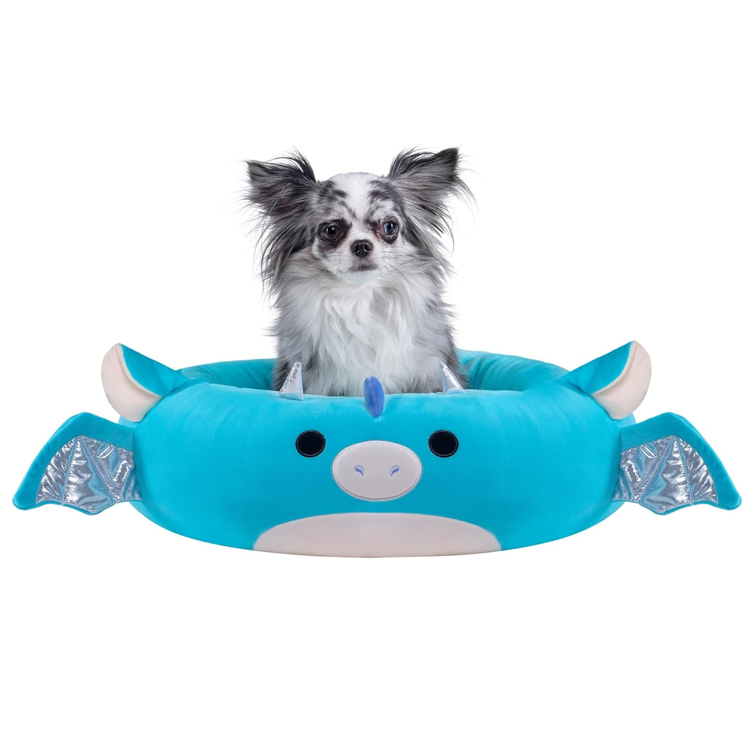 A small dog sits in a plush, blue dragon-shaped pet bed with silver wing details and cartoon-like facial features.