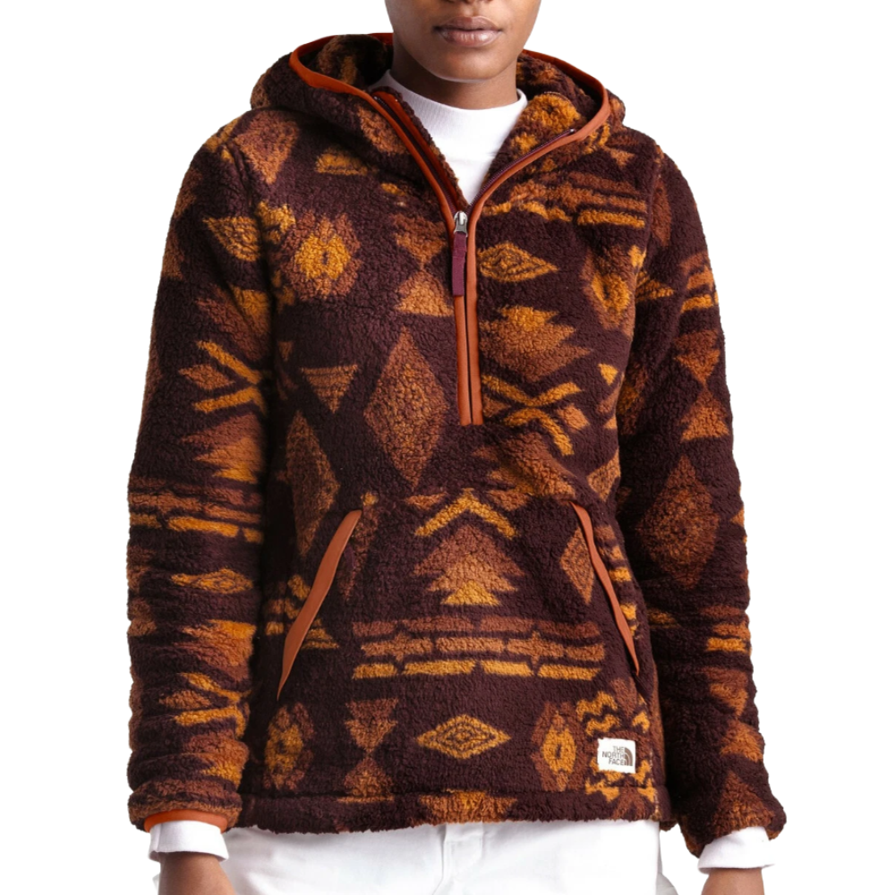 A person wears a fleece pullover hoodie with a geometric tribal pattern in shades of brown and orange, featuring a front kangaroo pocket and partial zip front.
