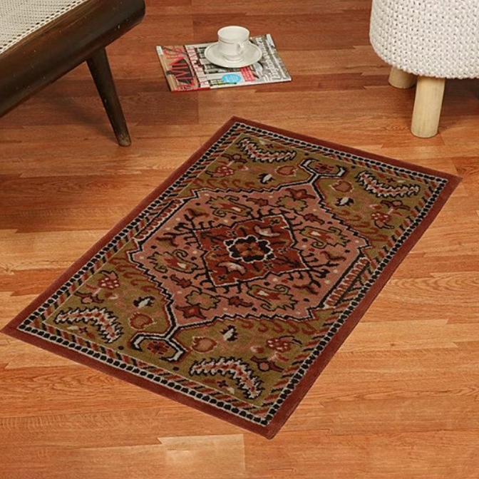 A small, rectangular hand-tufted rug with a traditional geometric pattern in earthy colors, placed on a wooden floor near a chair. A magazine and a teacup on a saucer are nearby.
