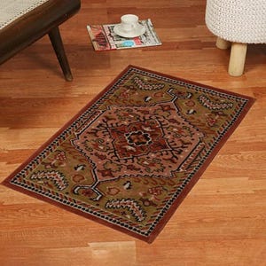 A small, rectangular hand-tufted rug with a traditional geometric pattern in earthy colors, placed on a wooden floor near a chair. A magazine and a teacup on a saucer are nearby.