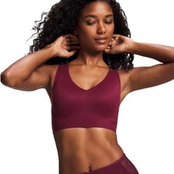 A woman poses wearing a burgundy sports bra, featuring a V-neck design with a smooth, seamless finish.
