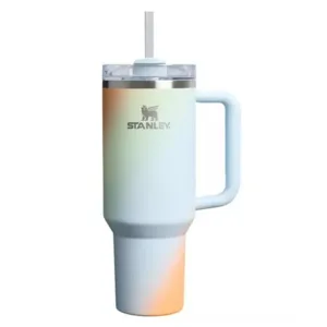 A Stanley tumbler with a gradient design featuring hues of blue, orange, and yellow, equipped with a handle, lid, and straw.
