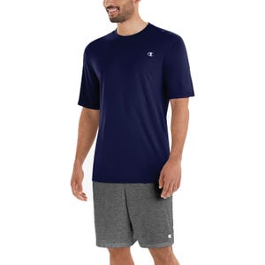 A man wearing a navy blue T-shirt and gray shorts, both featuring a small logo on the chest and pant leg.