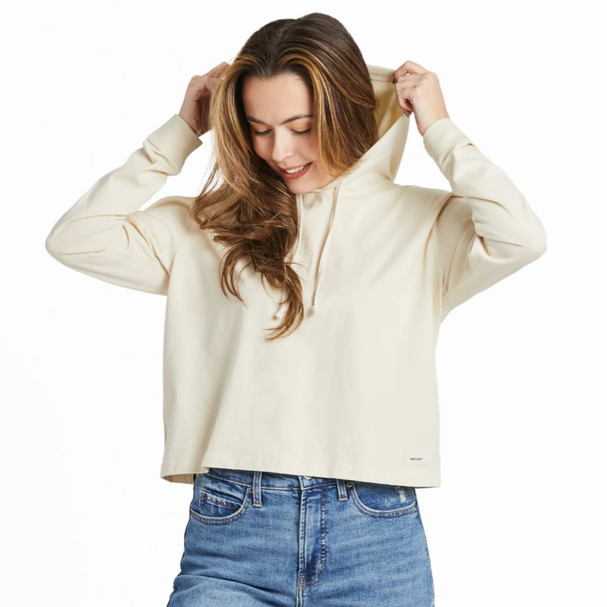 A person wearing a cream-colored hoodie with a relaxed fit, paired with blue jeans, adjusting the hood.