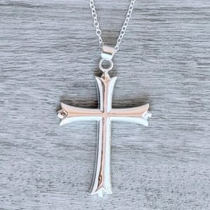 A silver cross pendant with a beveled design hangs on a chain against a textured gray background.