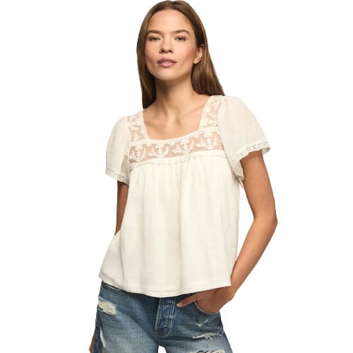 A woman is wearing a white blouse with lace detailing on the upper portion and short sleeves, paired with distressed denim jeans.