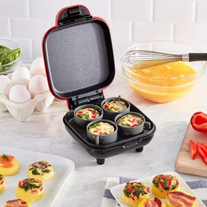 A mini pancake maker with batter and fillings, and prepared egg bites on a plate.