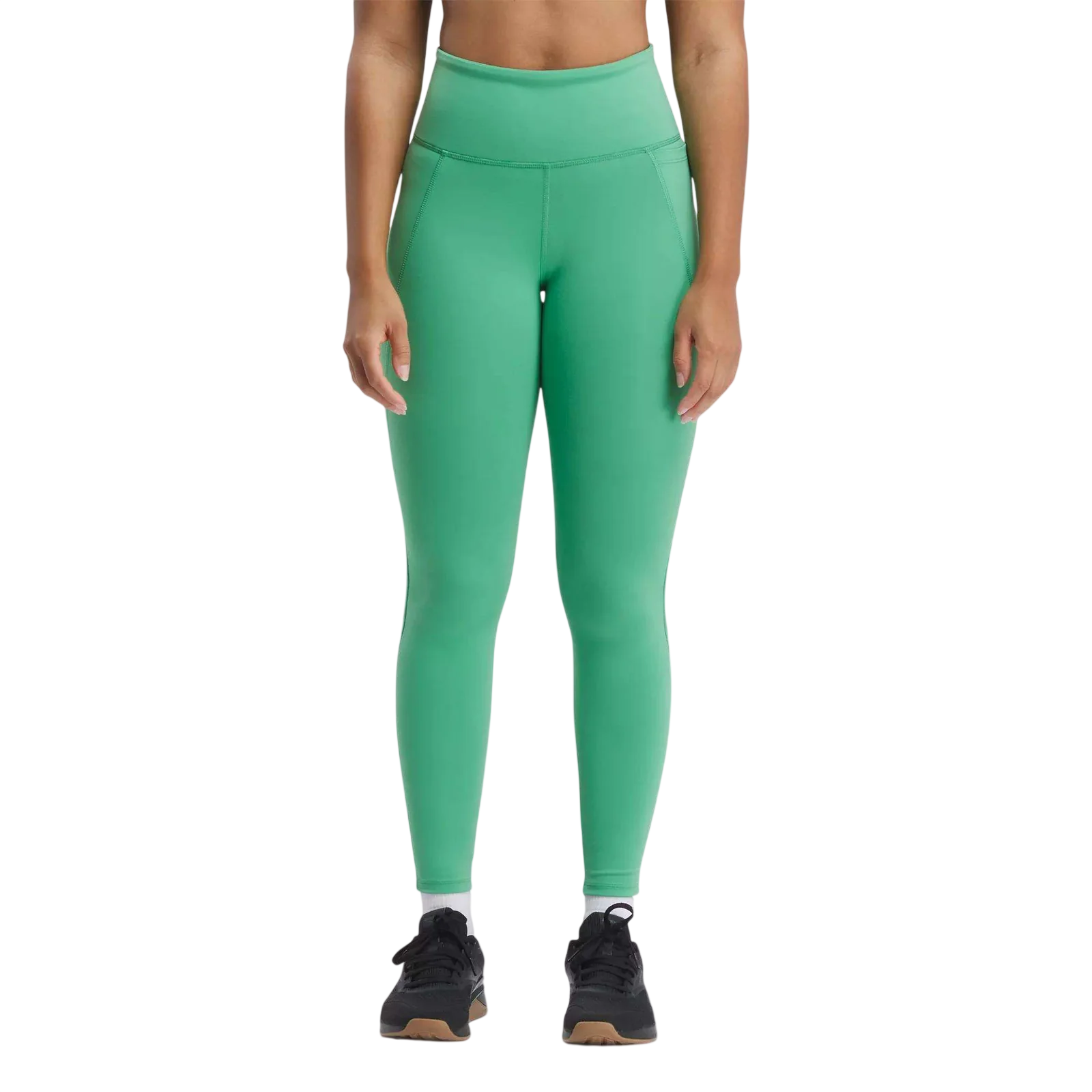 A person wears high-waisted green leggings with black athletic shoes, featuring a wide waistband and seam details.