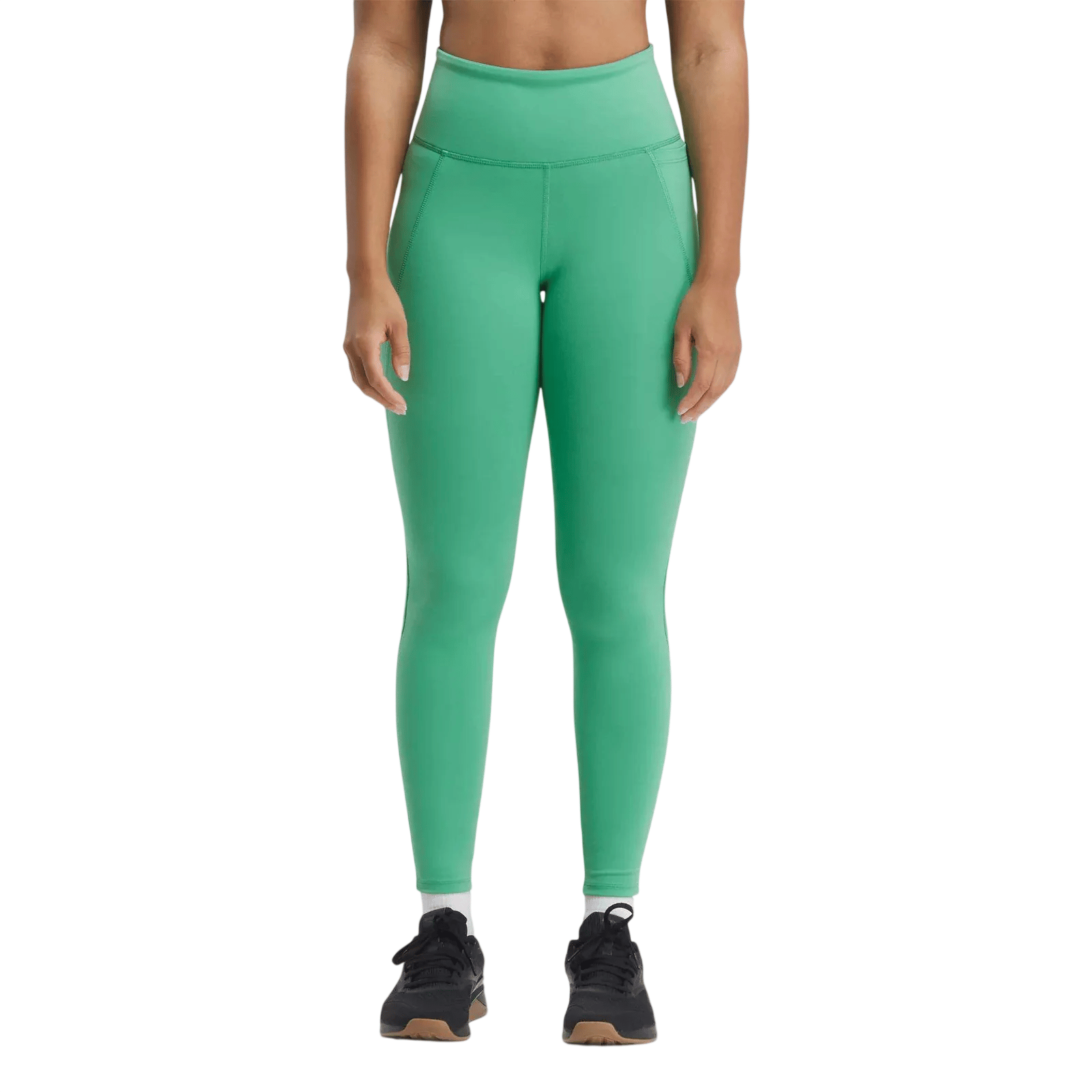 A person wears high-waisted green leggings with black athletic shoes, featuring a wide waistband and seam details.
