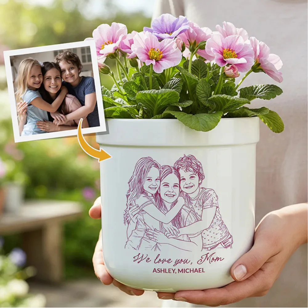A personalized flower pot with a line drawing of a mother and two children, based on the included photo, has \“We love you, Mom\“ along with \“Ashley, Michael.\“ Purple and pink flowers are planted in it.