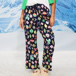 Person wearing navy pajama pants with colorful holiday ornament patterns, paired with a green cardigan and fluffy slippers, set against a snowy mountain backdrop.