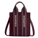 A Coach tote bag with a textured burgundy leather finish and wide straps featuring the Coach logo in white on a pink and black striped background.