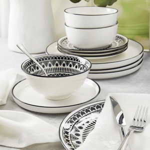 A set of white dinnerware with black geometric patterns, including bowls, plates, and a cup, accompanied by silver cutlery and a white napkin.