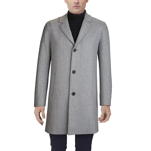 A grey Cole Haan men's topcoat featuring a minimalist design with a three-button front closure, notched lapels, and long sleeves, paired with a black turtleneck sweater and dark trousers.